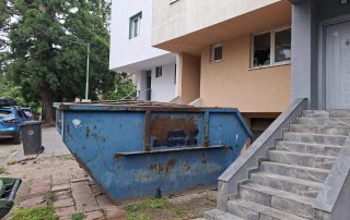 Син контейнер за строителни отпадъци до вход на жилищна сграда